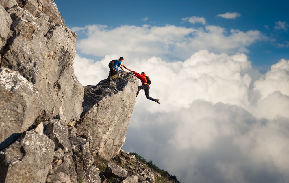 Two climbers ascending a majestic mountain peak against a backdrop of clouds, symbolizing the thrill of adventure and commitment to safety.